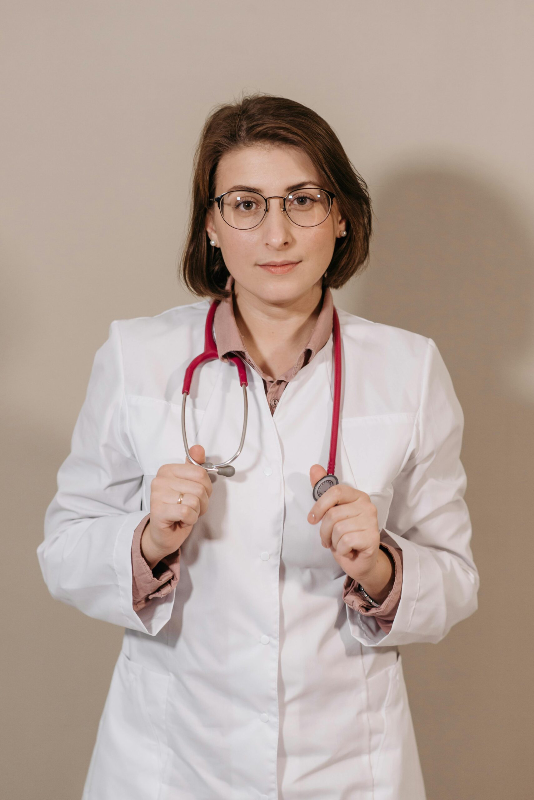 A professional female doctor posing confidently with a stethoscope in a neutral background.